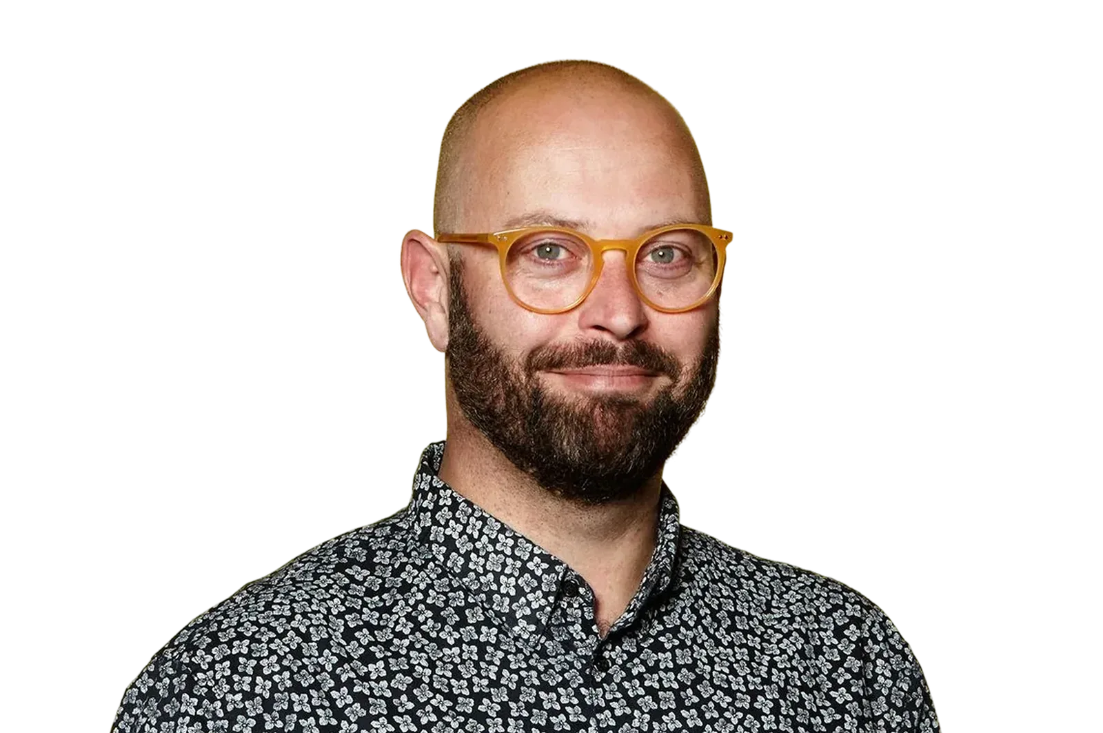 Smiling bald man with a beard wearing amber-colored round glasses and a black shirt with white floral patterns.