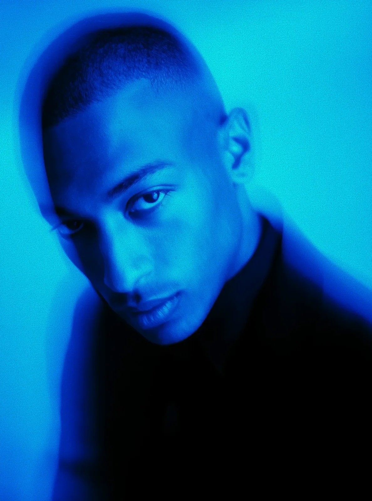 Close-up portrait of a man with short hair in blue lighting and a blurred effect.